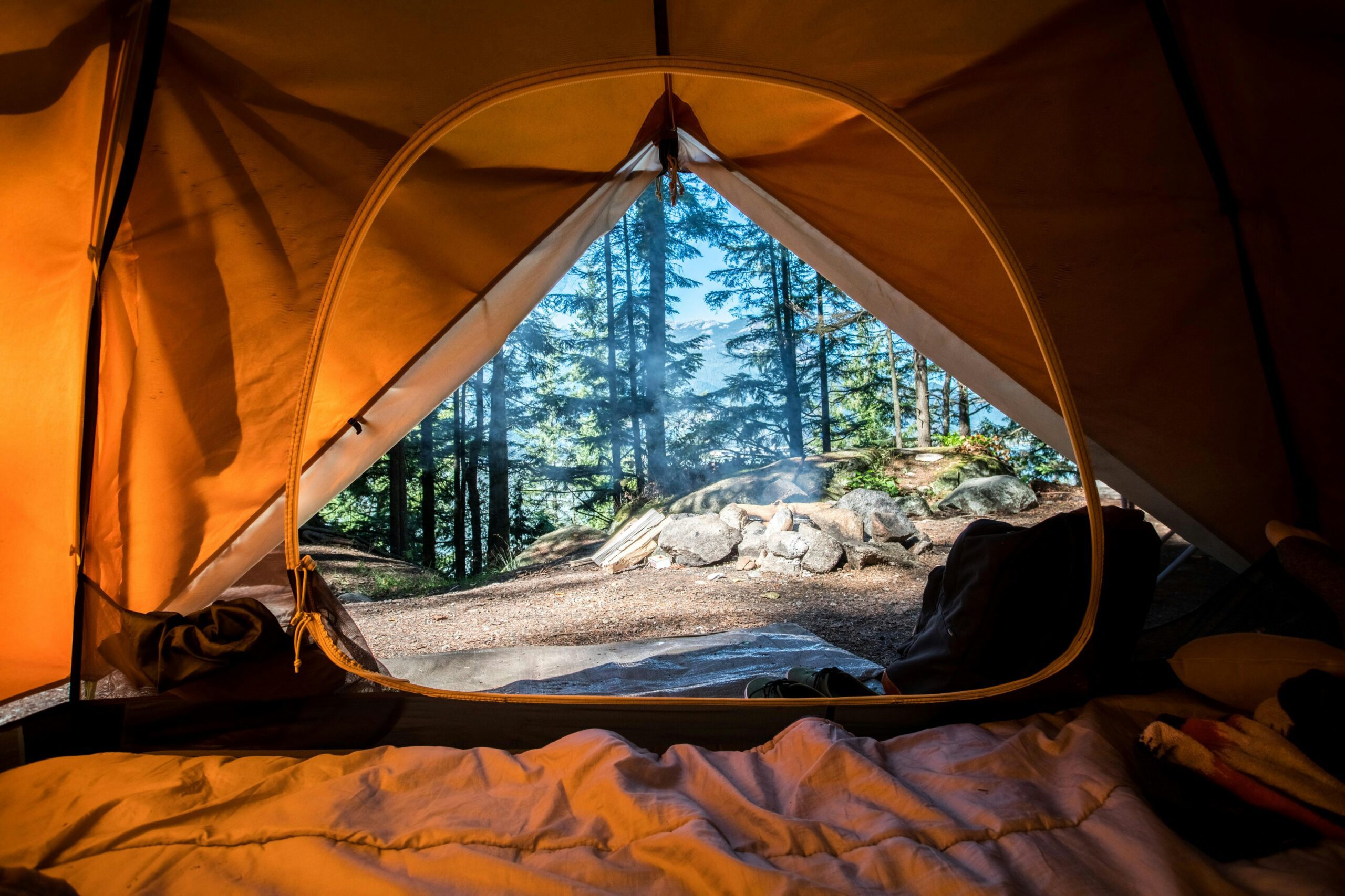 An orange-brown tent with the door open, looking out onto a woodland clearing with a large rock. This symbolizes how some people thrive outdoors.